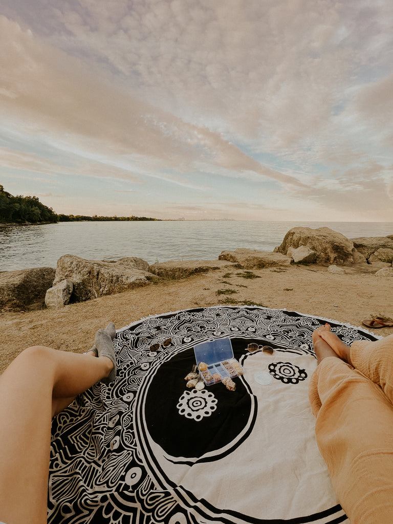 Karina and Nikita with their legs on the Harmony Mandala Throw, relaxing, making jewelry by the water looking at the sunset.