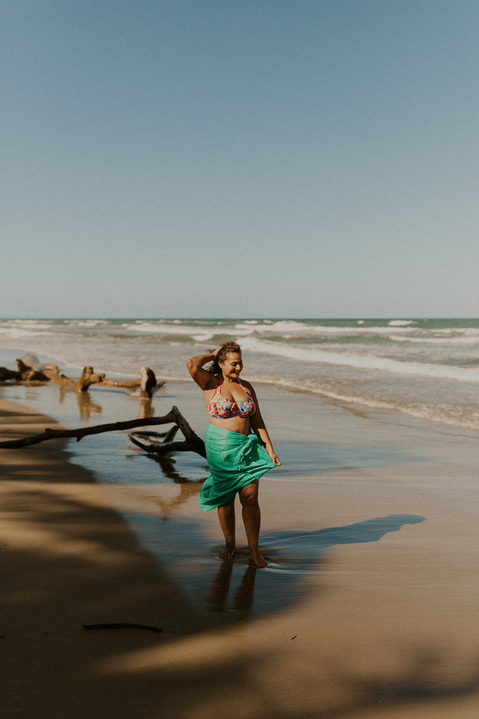 Woman wearing Kaiilani handloom towel in Mélon wrapped around her waist, walking on the beach.