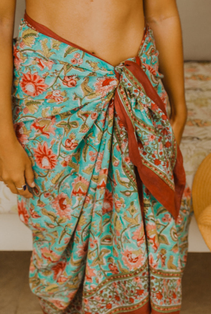 Close up of Kaiilani Manzanillo blockprint sarong with rust, turquoise and pink floral pattern on it.