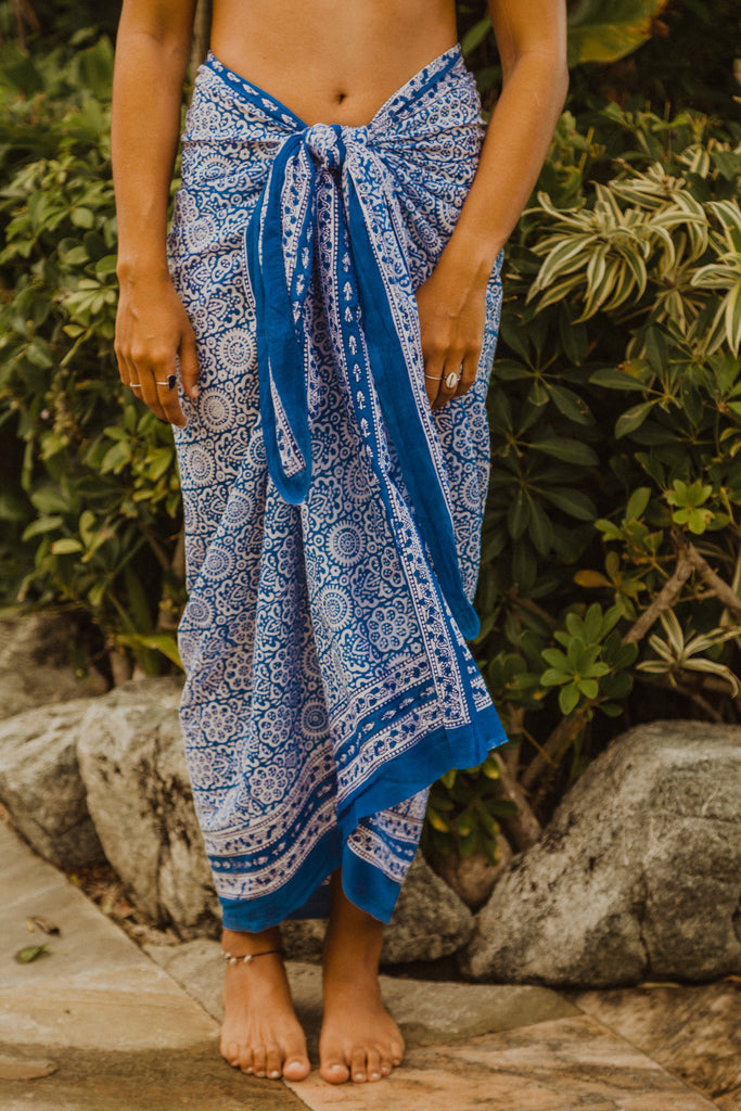Woman in front of plants with Kaiilani Santorini indigo and white blockprint sarong around her waist.