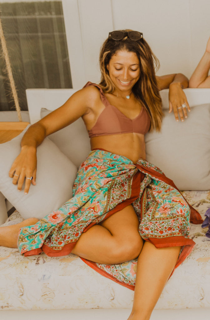 Women sitting on white swing wearing Kaiilani Manzanillo blockprint sarong with rust, turquoise and pink floral pattern on it.